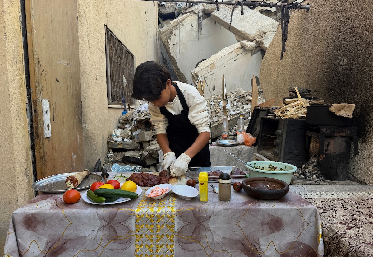 ياسر عياد، فتى فلسطيني يبلغ من العمر أربعة عشر عامًا، يمارس مهاراته في الطبخ على نار الحطب بجوار أنقاض منزل عائلته المدمر في مدينة غزة. غزة، 10 أبريل/نيسان 2026. تصوير: محمد الأسود