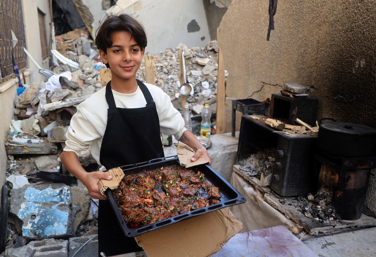 ياسر عياد، فتى فلسطيني يبلغ من العمر أربعة عشر عامًا، يمارس مهاراته في الطبخ على نار الحطب بجوار أنقاض منزل عائلته المدمر في مدينة غزة. غزة، 10 أبريل/نيسان 2026. تصوير: محمد الأسود
