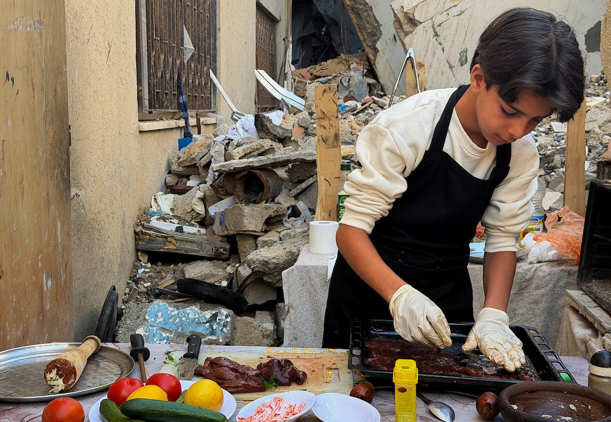ياسر عياد، فتى فلسطيني يبلغ من العمر أربعة عشر عامًا، يمارس مهاراته في الطبخ على نار الحطب بجوار أنقاض منزل عائلته المدمر في مدينة غزة. غزة، 10 أبريل/نيسان 2026. تصوير: محمد الأسود
