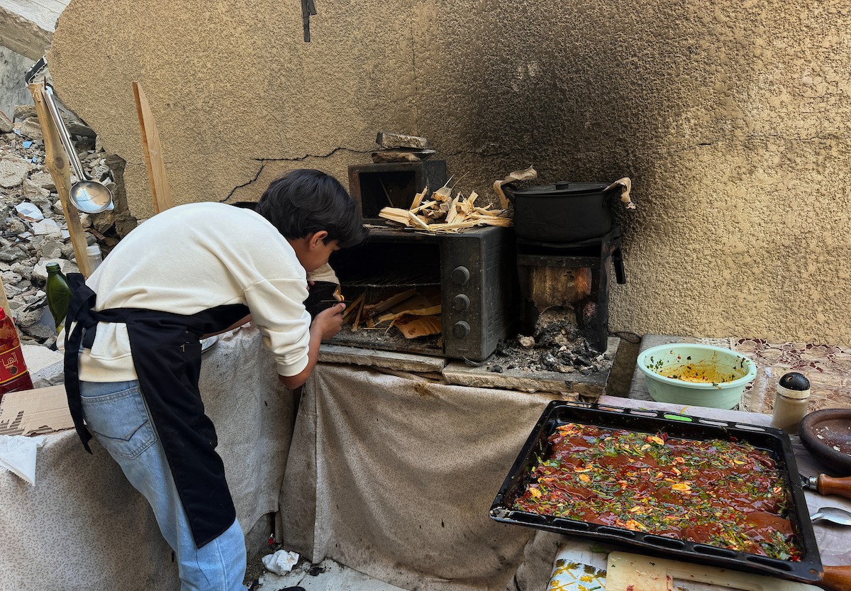 ياسر عياد، فتى فلسطيني يبلغ من العمر أربعة عشر عامًا، يمارس مهاراته في الطبخ على نار الحطب بجوار أنقاض منزل عائلته المدمر في مدينة غزة. غزة، 10 أبريل/نيسان 2026. تصوير: محمد الأسود
