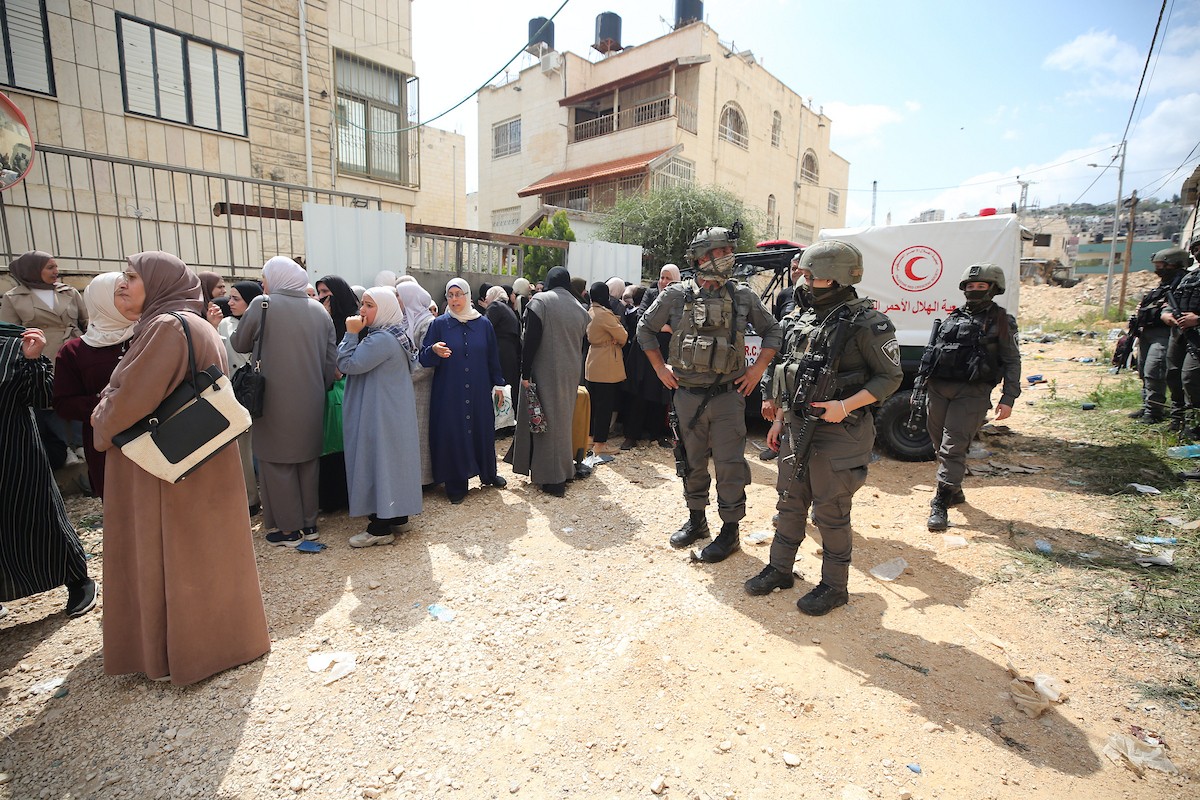 عائلات فلسطينية تنتظر عند نقطة تفتيش تابعة للجيش الإسرائيلي عند مدخل مخيم جنين للاجئين، قرب مدينة جنين في الضفة الغربية، لاستعادة ممتلكاتها من منازلها، 13 أبريل/نيسان 2026. صورة: محمد ناصر