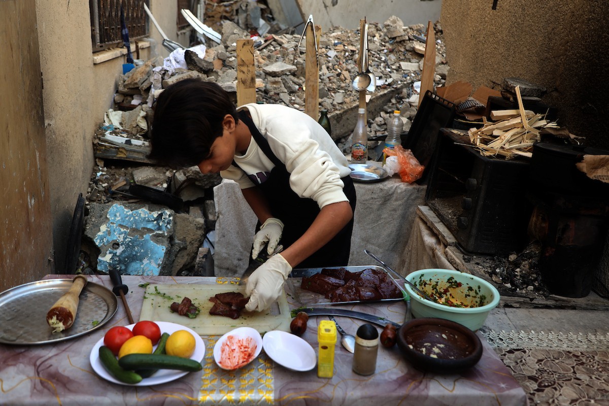 ياسر عياد، فتى فلسطيني يبلغ من العمر أربعة عشر عامًا، يمارس مهاراته في الطبخ على نار الحطب بجوار أنقاض منزل عائلته المدمر في مدينة غزة. غزة، 10 أبريل/نيسان 2026. تصوير: محمد الأسود