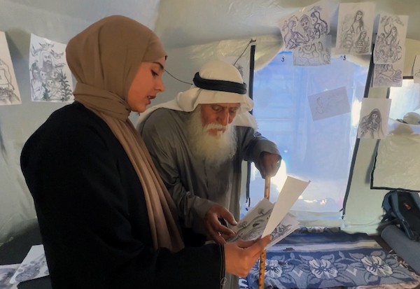 محمد زملط، رجل فلسطيني مسنّ اقتلعته الحرب من مخيم جباليا في شمال قطاع غزة، يحمل اليوم ريشته كوسيلة للبقاء، لا للفن فقط. في خيمته المتواضعة بمخيم البريج وسط القطاع، 12 أبريل/نيسان 2026، عدسة: يوسف أبو وطفة