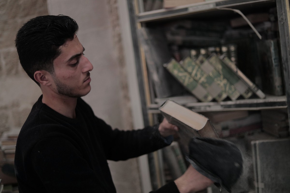 يتردد الشاب الفلسطيني كريم الخضري على مكتبة الجامع الكبير بغزة (الجامع العمري) في البلدة القديمة، شرق مدينة غزة، حيث يقوم بتنظيف الكتب وترتيبها بجدٍّ واجتهاد، 26 أبريل/نيسان 2026. تصوير: محمد الأسود