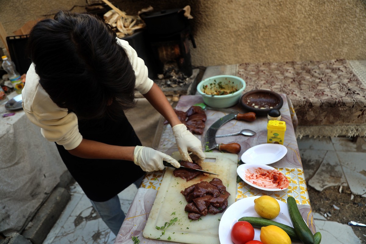ياسر عياد، فتى فلسطيني يبلغ من العمر أربعة عشر عامًا، يمارس مهاراته في الطبخ على نار الحطب بجوار أنقاض منزل عائلته المدمر في مدينة غزة. غزة، 10 أبريل/نيسان 2026. تصوير: محمد الأسود