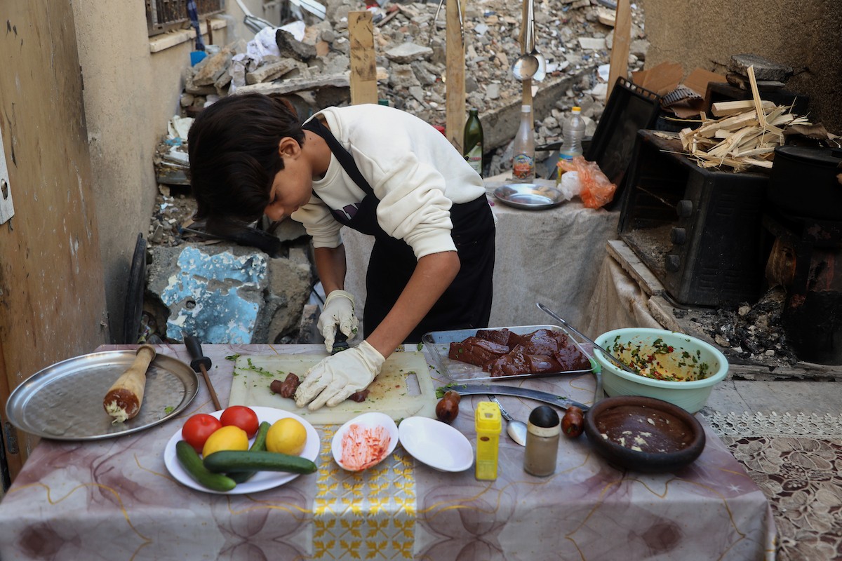 ياسر عياد، فتى فلسطيني يبلغ من العمر أربعة عشر عامًا، يمارس مهاراته في الطبخ على نار الحطب بجوار أنقاض منزل عائلته المدمر في مدينة غزة. غزة، 10 أبريل/نيسان 2026. تصوير: محمد الأسود
