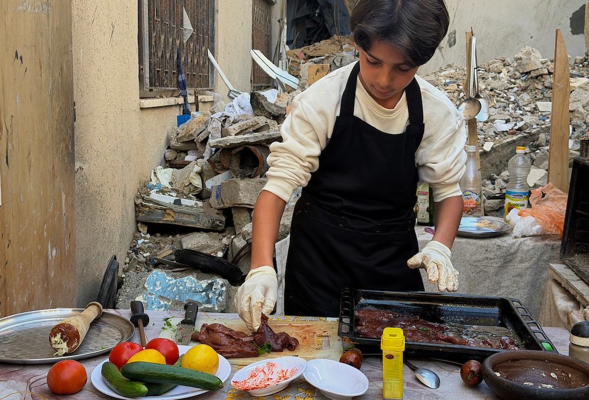 ياسر عياد، فتى فلسطيني يبلغ من العمر أربعة عشر عامًا، يمارس مهاراته في الطبخ على نار الحطب بجوار أنقاض منزل عائلته المدمر في مدينة غزة. غزة، 10 أبريل/نيسان 2026. تصوير: محمد الأسود