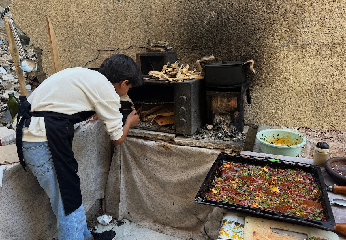 ياسر عياد، فتى فلسطيني يبلغ من العمر أربعة عشر عامًا، يمارس مهاراته في الطبخ على نار الحطب بجوار أنقاض منزل عائلته المدمر في مدينة غزة. غزة، 10 أبريل/نيسان 2026. تصوير: محمد الأسود