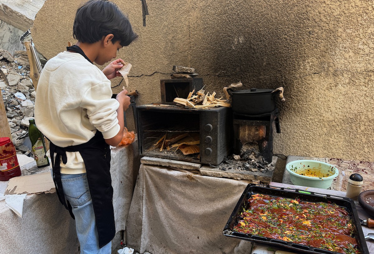 ياسر عياد، فتى فلسطيني يبلغ من العمر أربعة عشر عامًا، يمارس مهاراته في الطبخ على نار الحطب بجوار أنقاض منزل عائلته المدمر في مدينة غزة. غزة، 10 أبريل/نيسان 2026. تصوير: محمد الأسود
