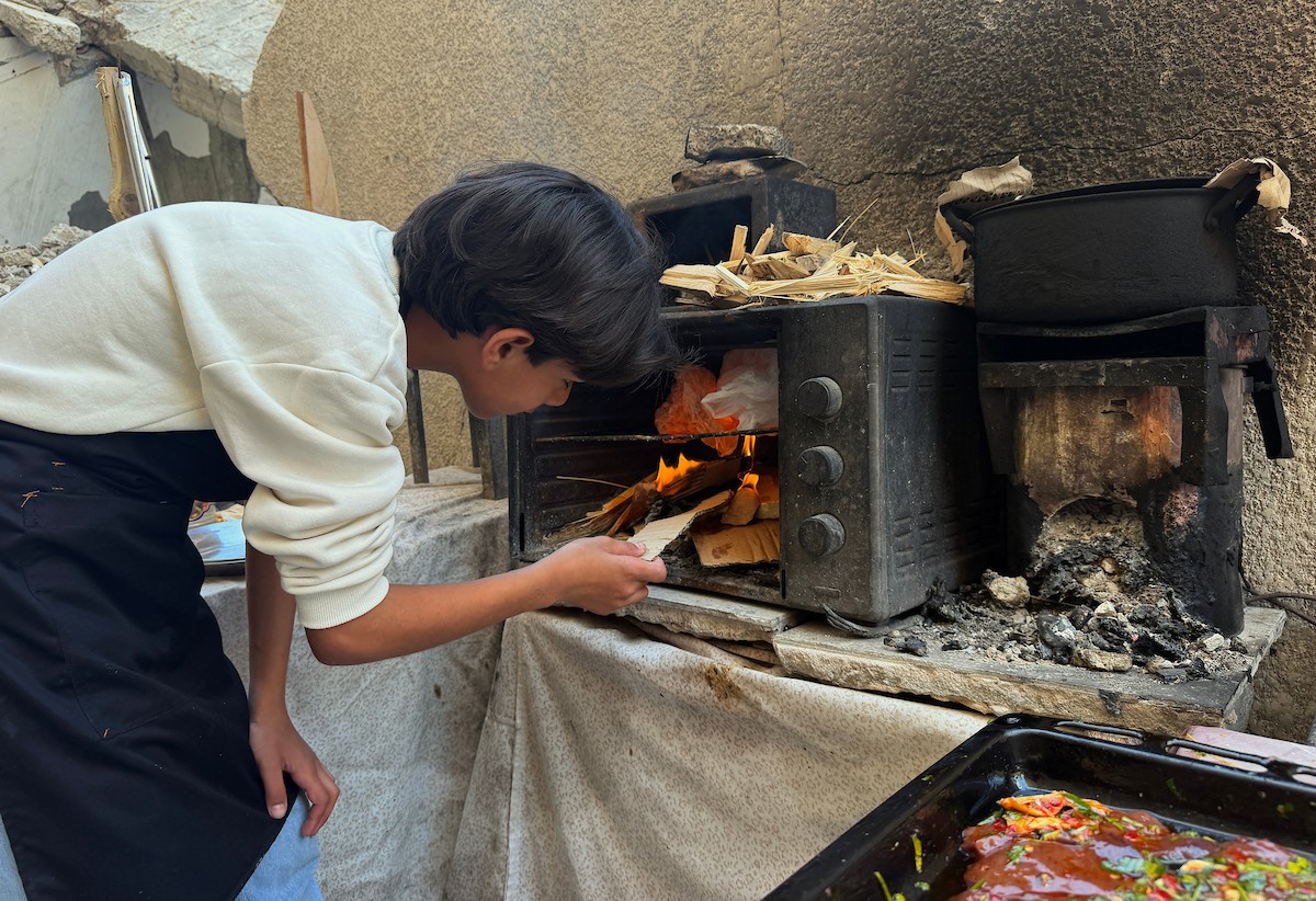 ياسر عياد، فتى فلسطيني يبلغ من العمر أربعة عشر عامًا، يمارس مهاراته في الطبخ على نار الحطب بجوار أنقاض منزل عائلته المدمر في مدينة غزة. غزة، 10 أبريل/نيسان 2026. تصوير: محمد الأسود