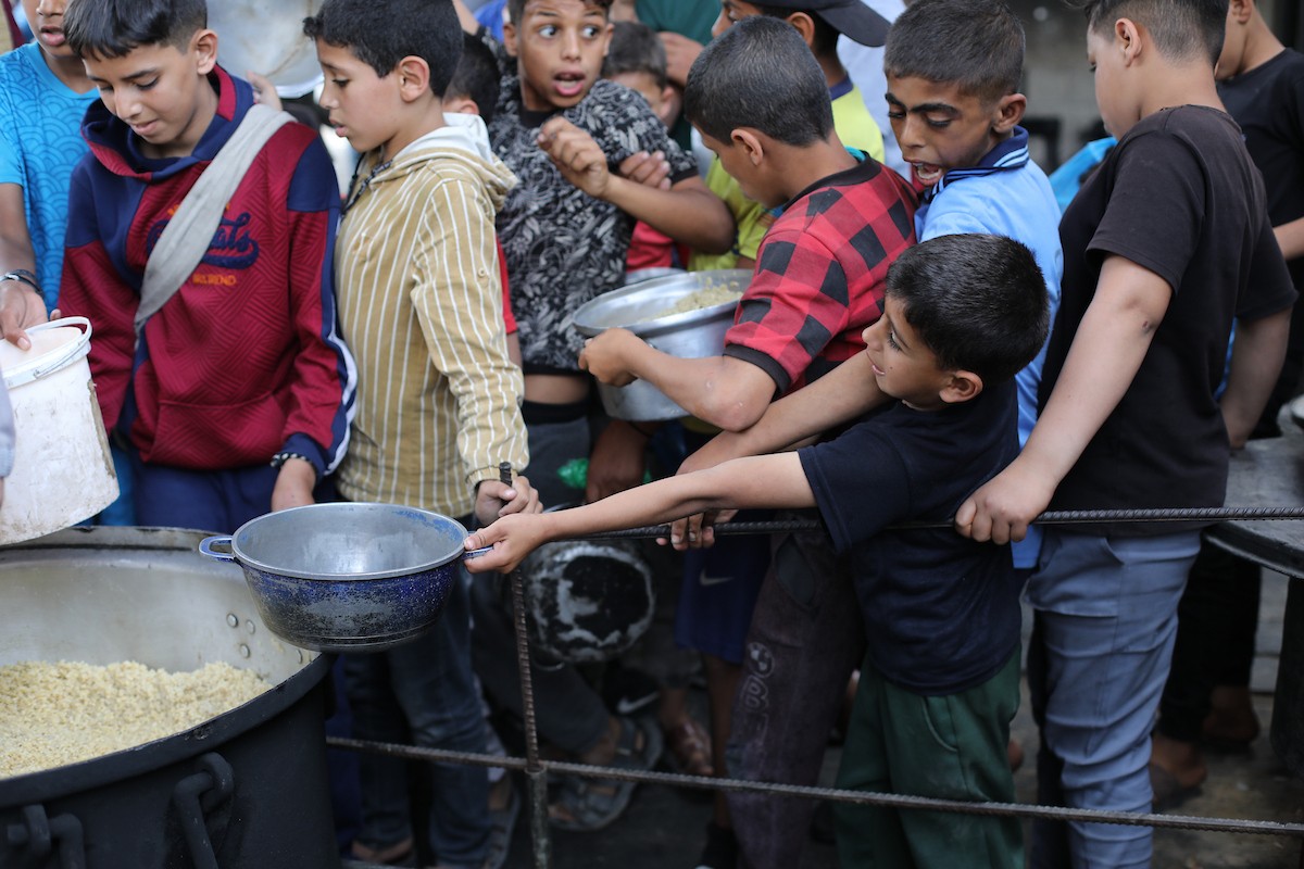 فلسطينيون نازحون، بينهم نساء وأطفال، يتجمعون لتلقي وجبات طعام من مطبخ خيري في مخيم النصيرات للاجئين وسط قطاع غزة، في 18 مايو/أيار 2026، وسط تراجع الإمدادات الإنسانية وخفض توزيع الوجبات اليومية من قبل منظمة «وورلد سنترال كيتشن». الصورة: حسن الجديدي