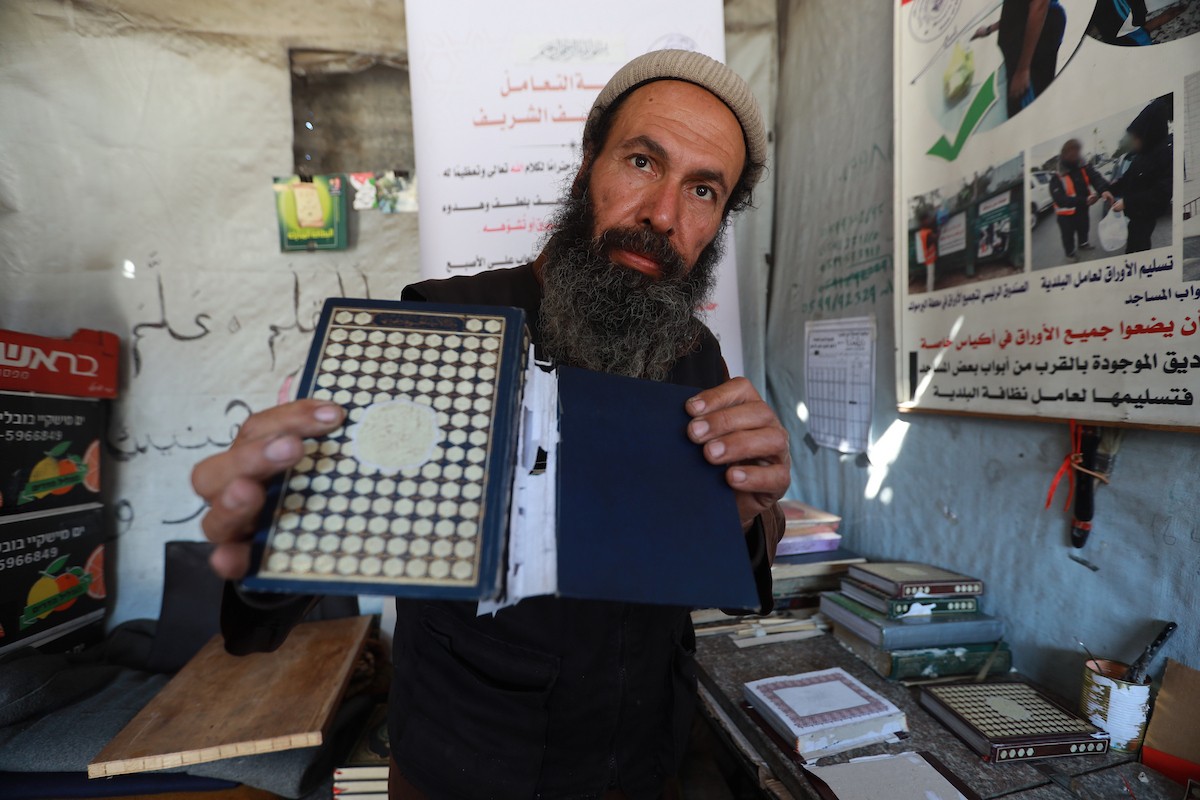 المسنّ الفلسطيني رفعت جبر يرمم نسخ تالفة من المصحف الشريف، عُثر عليها بين أنقاض المساجد والمنازل التي دُمّرت خلال الهجمات الإسرائيلية في مدينة غزة، 5 مايو/أيار 2026 (صورة: عمر أشتوي)
