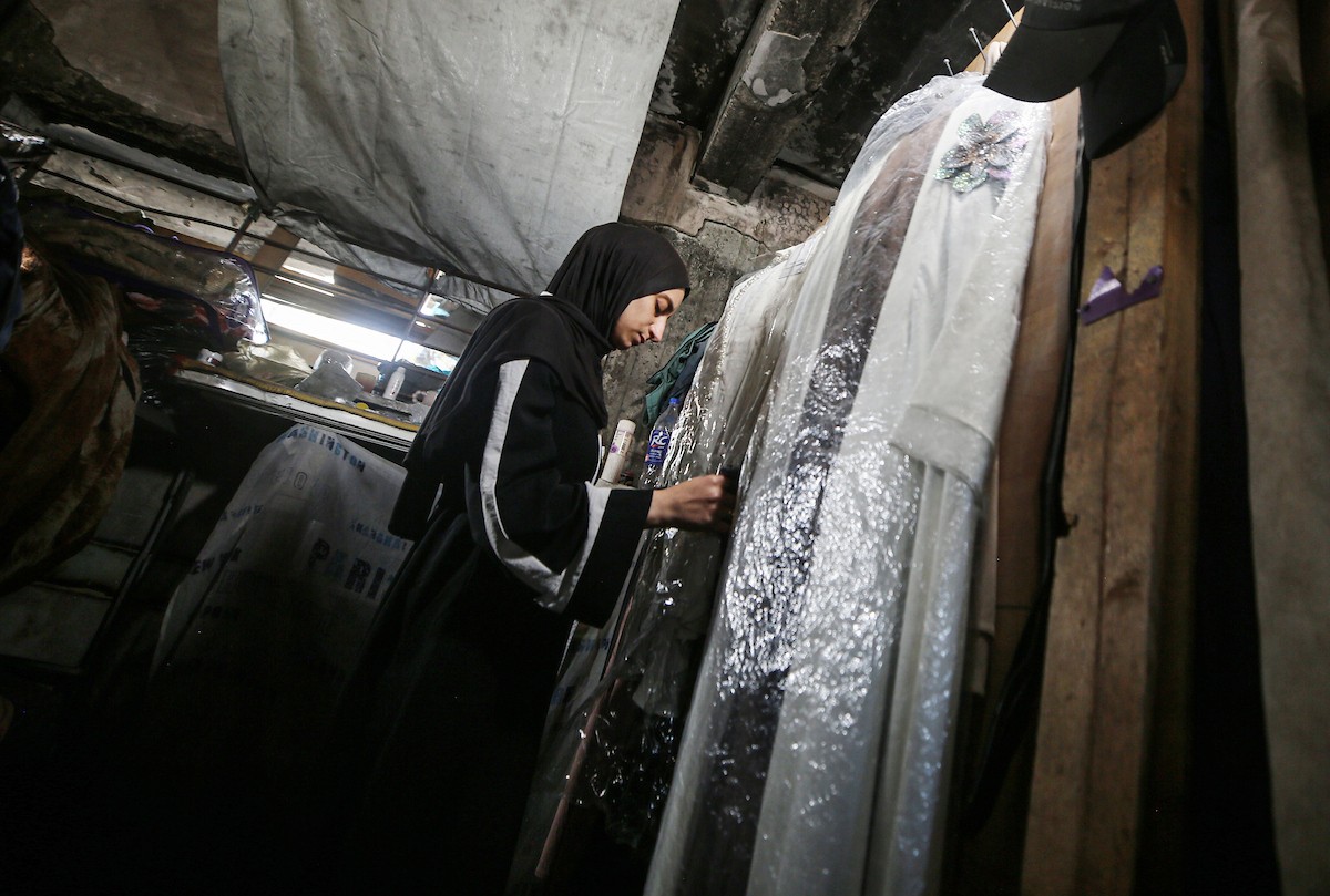 لينا مقداد، عروس فلسطينية، تنظر إلى صور ومقتنيات والدها بجانب فستان زفافها داخل مدرسة  تحُِّلت إلى مأوى للنازحين، في حي الشيخ رضوان بمدينة غزة، في 3 مايو/أيار 2026. فقدت مقداد والدها، عماد مقداد، في هجمات إسرائيلية على غزة قبل أسبوعين من زفافها