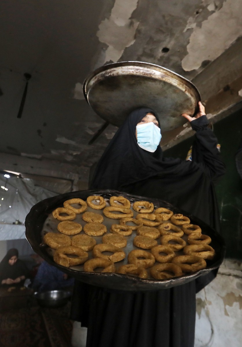 نساء فلسطينيات يُجهّزن ويخبزن كعكات العيد التقليدية على أفران مؤقتة داخل مأوى قرب منطقة “الخط الأصفر” شرق مدينة غزة، قبيل عيد الأضحى، 25 مايو/أيار 2026. تصوير: بلال أسامة