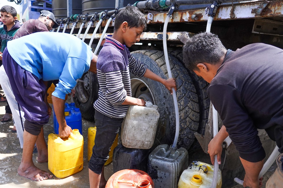 يحاول فلسطينيون نازحون، بينهم أطفال ونساء، جلب الماء من صهريج مياه متنقل في منطقة المواصي بخان يونس، جنوب قطاع غزة، 5 مايو/أيار 2026( صورة: رمزي أبو عامر)