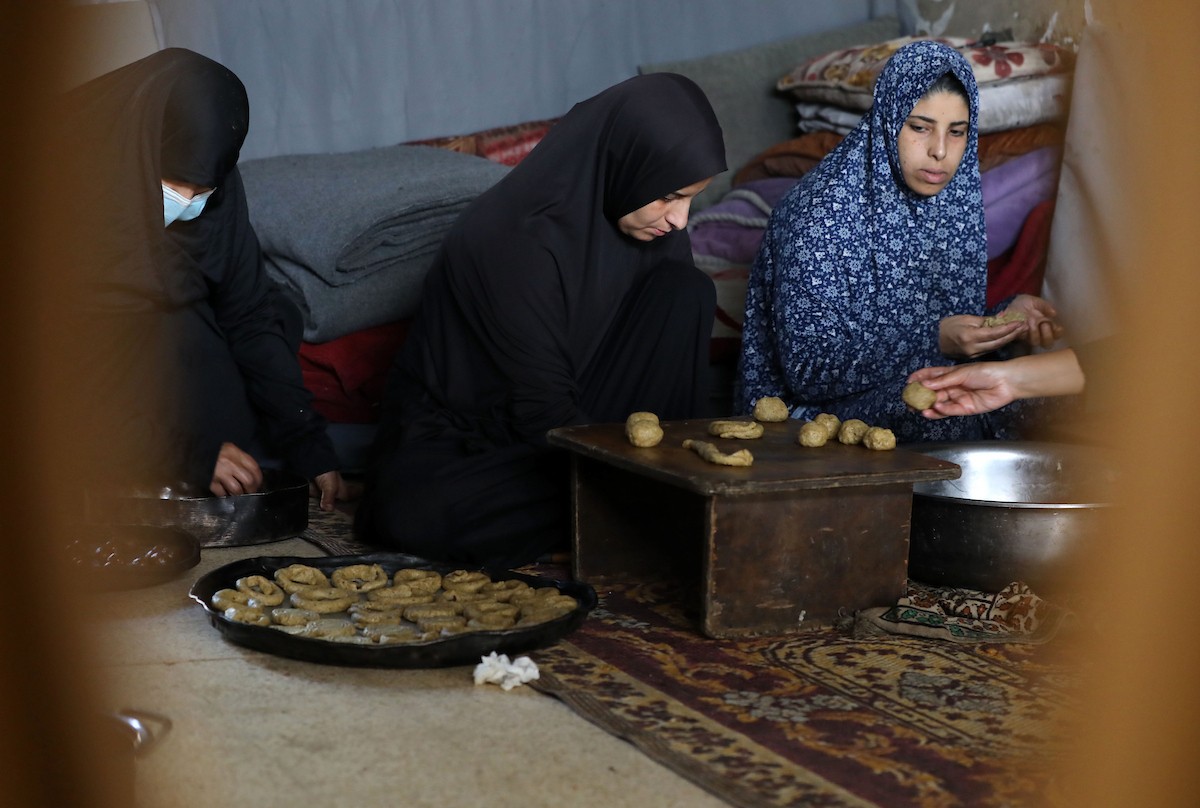 نساء فلسطينيات يُجهّزن ويخبزن كعكات العيد التقليدية على أفران مؤقتة داخل مأوى قرب منطقة “الخط الأصفر” شرق مدينة غزة، قبيل عيد الأضحى، 25 مايو/أيار 2026. تصوير: بلال أسامة