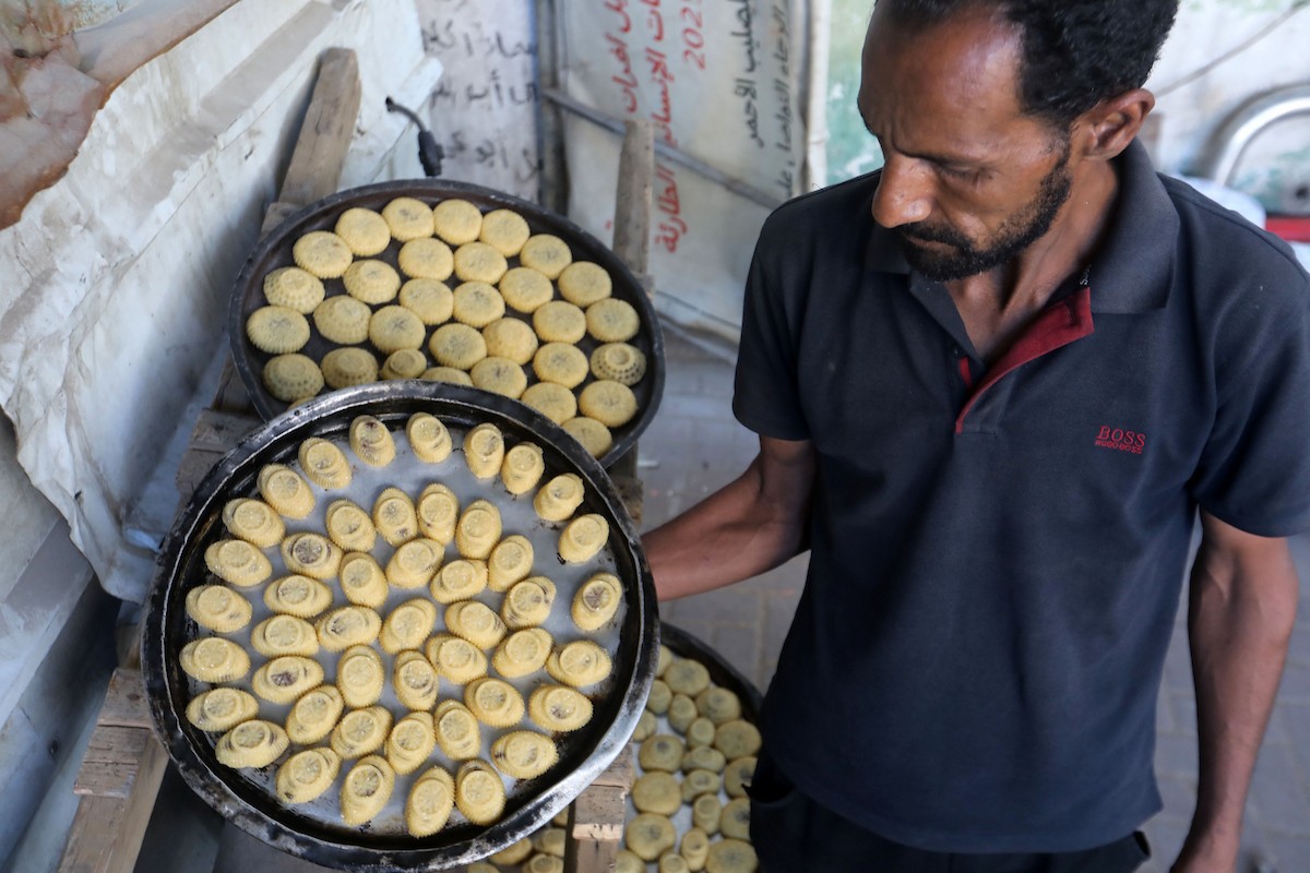 نساء فلسطينيات يُجهّزن ويخبزن كعكات العيد التقليدية على أفران مؤقتة داخل مأوى قرب منطقة “الخط الأصفر” شرق مدينة غزة، قبيل عيد الأضحى، 25 مايو/أيار 2026. تصوير: بلال أسامة
