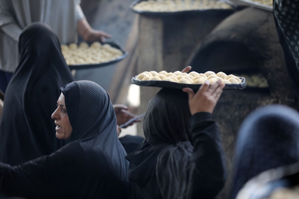 نساء فلسطينيات يُجهّزن ويخبزن كعكات العيد التقليدية على أفران مؤقتة داخل مأوى قرب منطقة “الخط الأصفر” شرق مدينة غزة، قبيل عيد الأضحى، 25 مايو/أيار 2026. تصوير: بلال أسامة