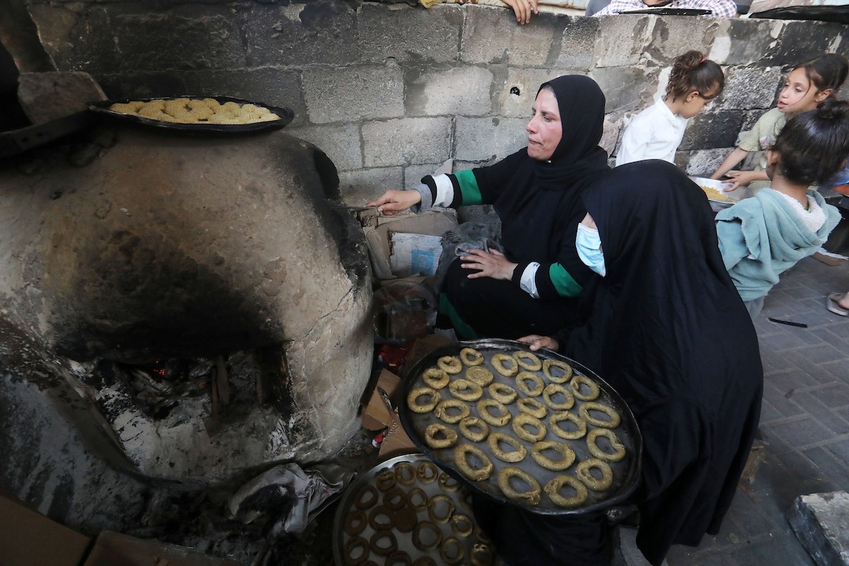 نساء فلسطينيات يُجهّزن ويخبزن كعكات العيد التقليدية على أفران مؤقتة داخل مأوى قرب منطقة “الخط الأصفر” شرق مدينة غزة، قبيل عيد الأضحى، 25 مايو/أيار 2026. تصوير: بلال أسامة