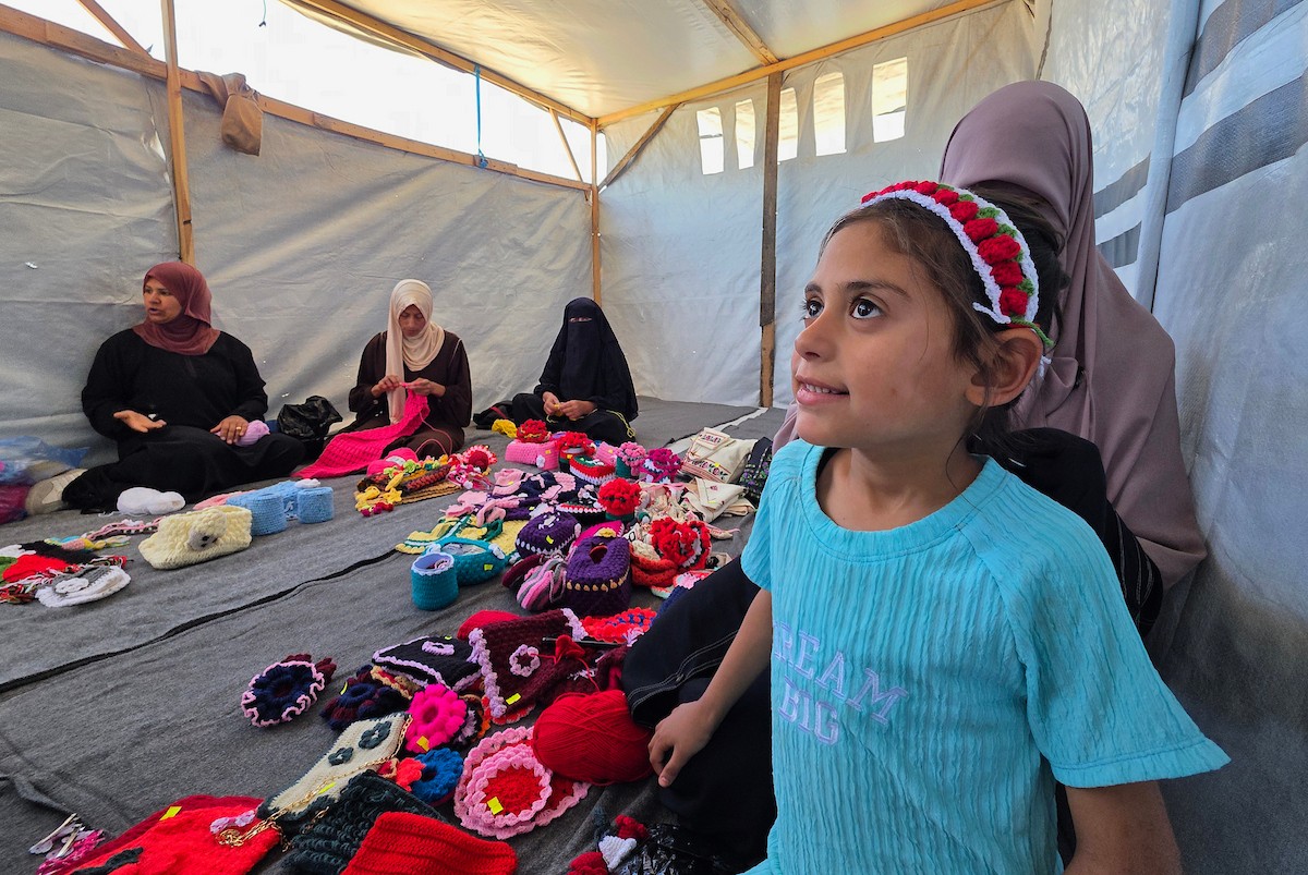 أرامل فلسطينيات يعملن على حياكة المشغولات الصوفية داخل خيمة في مخيم البركة للأيتام بمنطقة مواصي في خان يونس جنوب قطاع غزة، في 11 مايو/أيار 2026، سعياً منهن لتأمين دخل لإعالة أطفالهن بعد استشهاد أزواجهن في الحرب. (صورة: طارق محمد)
