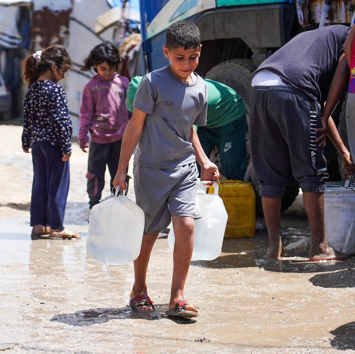 يحاول فلسطينيون نازحون، بينهم أطفال ونساء، جلب الماء من صهريج مياه متنقل في منطقة المواصي بخان يونس، جنوب قطاع غزة، 5 مايو/أيار 2026( صورة: رمزي أبو عامر)