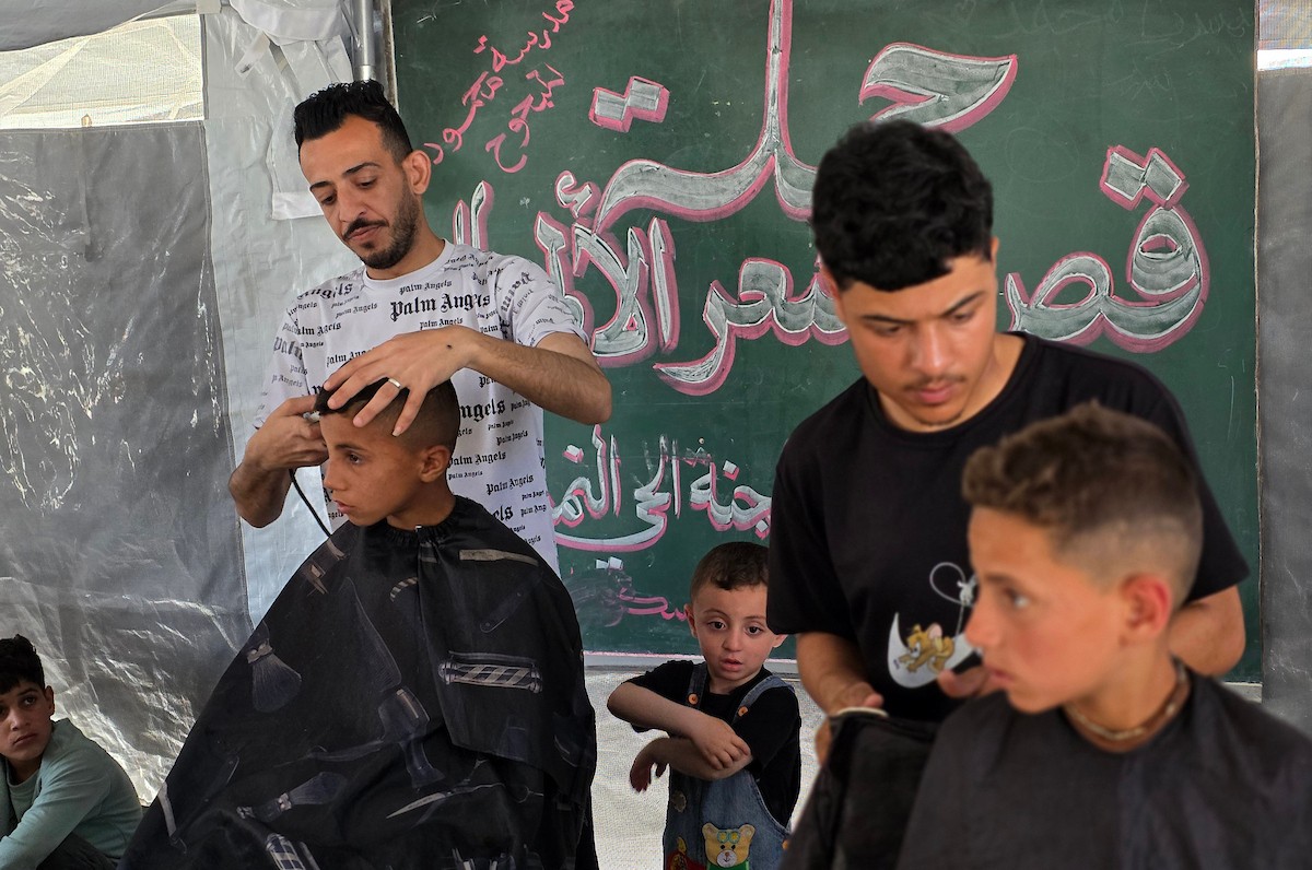 أطفال فلسطينيون نازحون يجلسون داخل خيمة لتلقي قصات شعر مجانية ضمن مبادرة شبابية تطوعية في خان يونس جنوب قطاع غزة، في 13 مايو/أيار 2026. وتهدف المبادرة إلى توفير قصات شعر لنحو ألف طفل نازح، تصوير: طارق محمد
