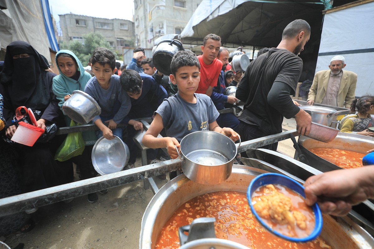 فلسطينيون بينهم نساء وأطفال يتلقون وجبات طعام من مطبخ خيري في النصيرات، وسط قطاع غزة، في 2 مايو/أيار 2026. (تصوير: حسن الجديدي)