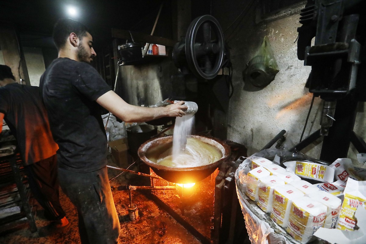 عمال فلسطينيون ينتجون حلوى “الحلقوم” التقليدية داخل مصنع متضرر في حي الدرج شرق مدينة غزة، قبيل عيد الأضحى المبارك، في 24 أيار/مايو 2026، بعد استئناف العمل بإمكانيات محدودة جراء أضرار الحرب وتراجع القدرة الشرائية للسكان. تصوير: بلال أسامة