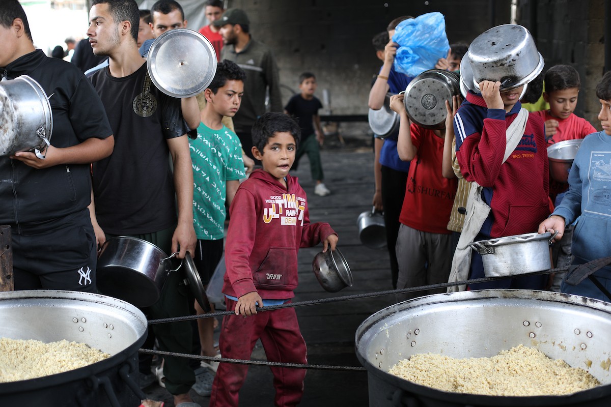 فلسطينيون نازحون، بينهم نساء وأطفال، يتجمعون لتلقي وجبات طعام من مطبخ خيري في مخيم النصيرات للاجئين وسط قطاع غزة، في 18 مايو/أيار 2026، وسط تراجع الإمدادات الإنسانية وخفض توزيع الوجبات اليومية من قبل منظمة «وورلد سنترال كيتشن». الصورة: حسن الجديدي