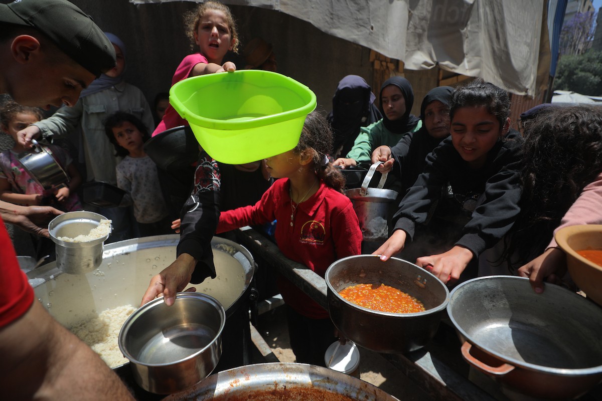 فلسطينيون نازحون، بينهم نساء وأطفال، يتجمعون لتلقي وجبات طعام من مطبخ خيري في مخيم النصيرات للاجئين وسط قطاع غزة، في 13 مايو/أيار 2026، وسط تراجع الإمدادات الإنسانية واستمرار الإغلاق الجزئي للمعابر الحدودية. تصوير: حسن الجديدي