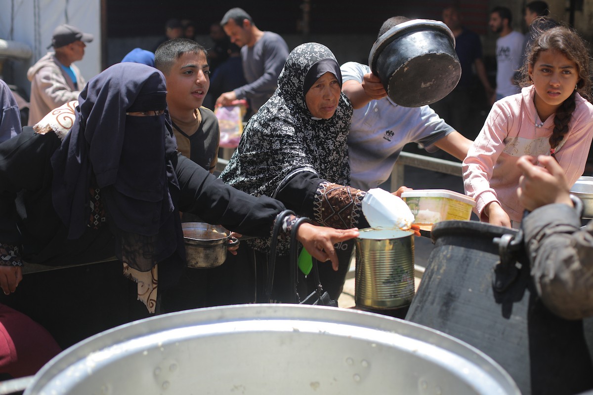 فلسطينيون نازحون، بينهم نساء وأطفال، يتجمعون لتلقي وجبات طعام من مطبخ خيري في مخيم النصيرات للاجئين وسط قطاع غزة، في 13 مايو/أيار 2026، وسط تراجع الإمدادات الإنسانية واستمرار الإغلاق الجزئي للمعابر الحدودية. تصوير: حسن الجديدي