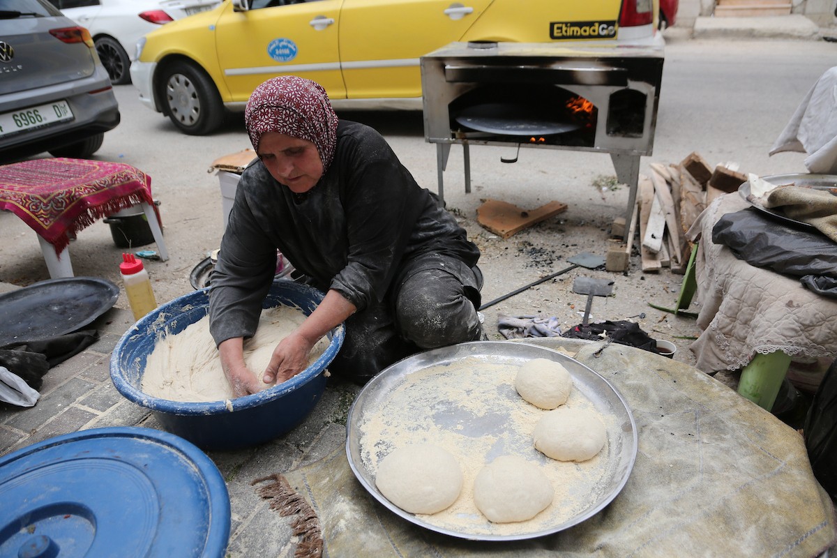امرأة فلسطينية تُعدّ الخبز على نار الحطب في شارع رئيسي بنابلس شمال الضفة الغربية، 2 مايو/أيار 2026، خلال معرض 