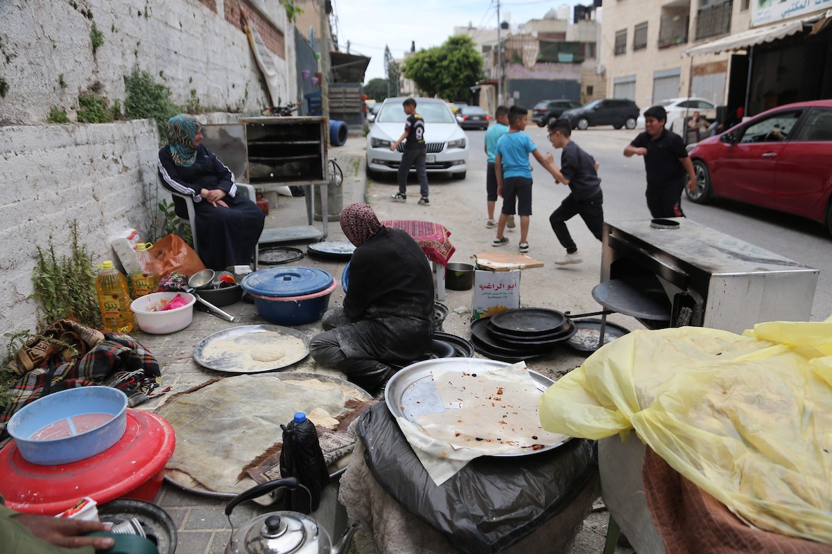 امرأة فلسطينية تُعدّ الخبز على نار الحطب في شارع رئيسي بنابلس شمال الضفة الغربية، 2 مايو/أيار 2026، خلال معرض 
