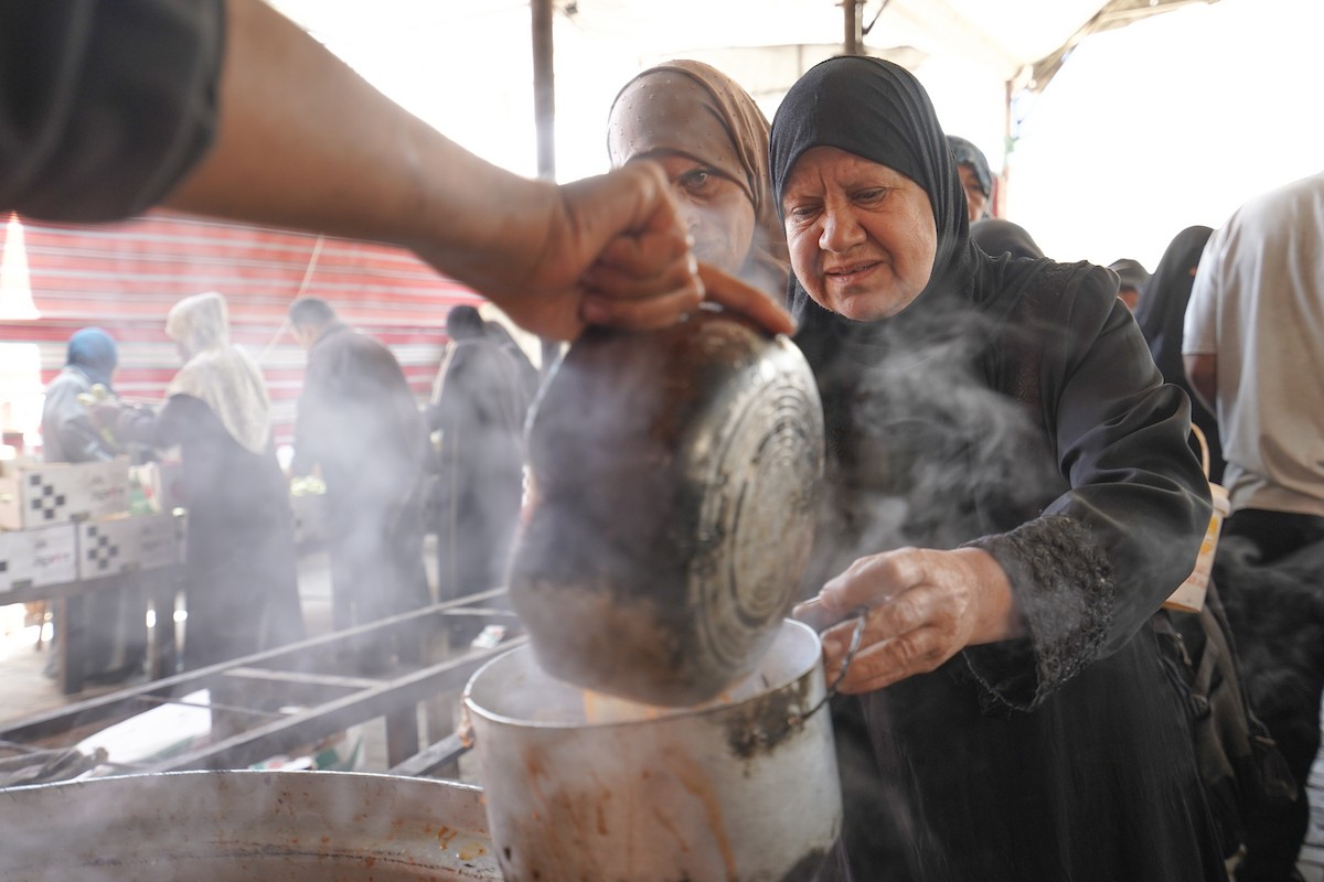 فلسطينيون نازحون، بينهم نساء وأطفال، يتجمعون لتلقي وجبات طعام من مطبخ خيري في مخيم النصيرات للاجئين وسط قطاع غزة، في 21 مايو/أيار 2026. الصورة: رمزي أبو عامر.