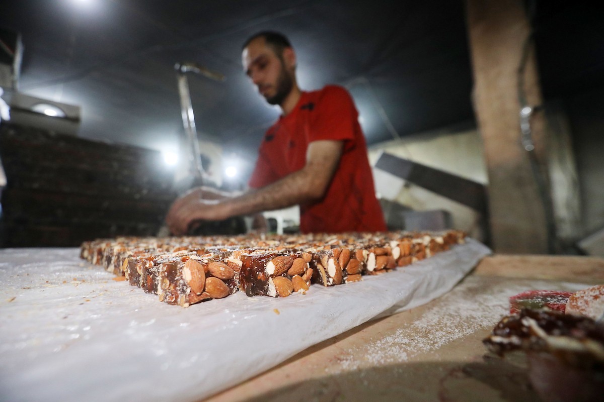 عمال فلسطينيون ينتجون حلوى “الحلقوم” التقليدية داخل مصنع متضرر في حي الدرج شرق مدينة غزة، قبيل عيد الأضحى المبارك، في 24 أيار/مايو 2026، بعد استئناف العمل بإمكانيات محدودة جراء أضرار الحرب وتراجع القدرة الشرائية للسكان. تصوير: بلال أسامة