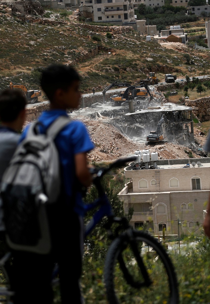 جرافات إسرائيلية تهدم مبنى سكنياً فلسطينياً قيد الإنشاء في بلدة الولجة غرب بيت لحم، في 18 مايو/أيار 2026، وسط انتشار قوات الاحتلال وتجمّع الأهالي لمتابعة عملية الهدم. الصورة: مأمون وزواز