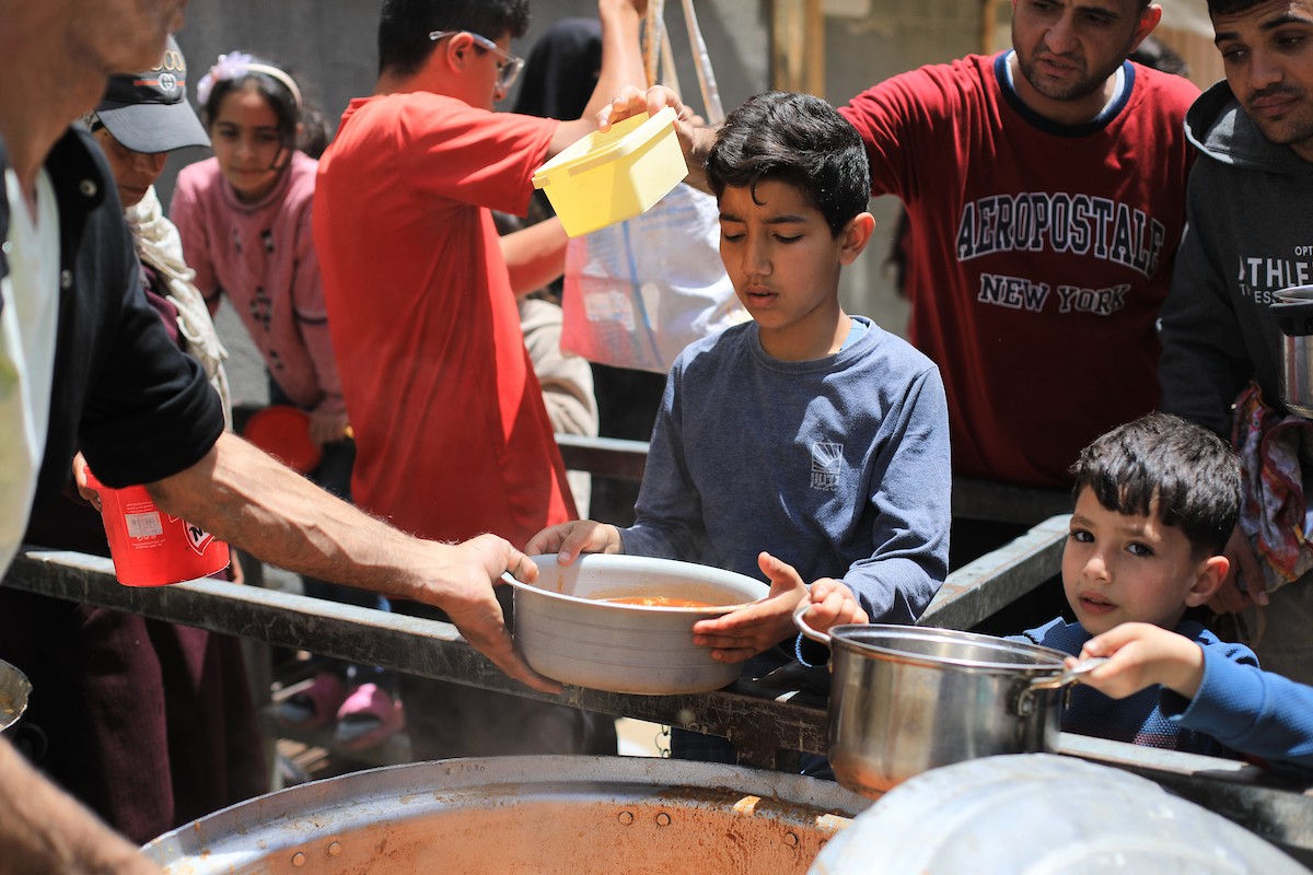 فلسطينيون بينهم نساء وأطفال يتلقون وجبات طعام من مطبخ خيري في النصيرات، وسط قطاع غزة، في 2 مايو/أيار 2026. (تصوير: حسن الجديدي)