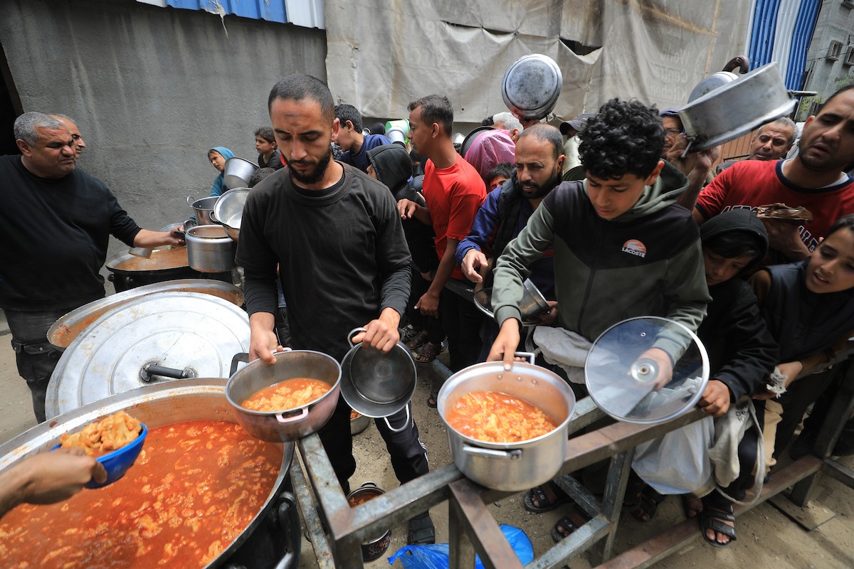 فلسطينيون بينهم نساء وأطفال يتلقون وجبات طعام من مطبخ خيري في النصيرات، وسط قطاع غزة، في 2 مايو/أيار 2026. (تصوير: حسن الجديدي)