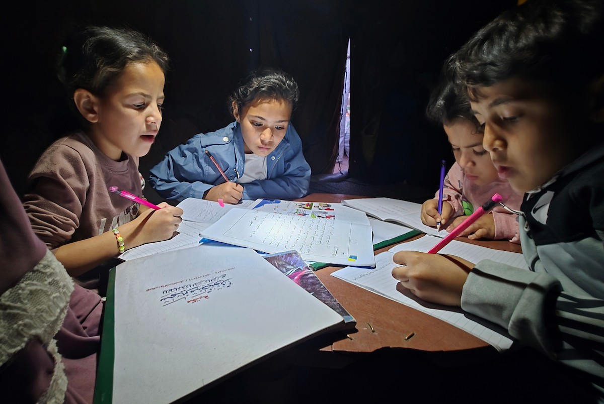 3 مايو/أيار 2026، الأم الفلسطينية ميساء حمدي تعليم أطفالها وأبناء أخيها الذين فقدوا والدتهم، على ضوء مصباح داخل خيمة في منطقة مواصي خان يونس، جنوب قطاع غزة. ويواجه سكان القطاع ظروفًا معيشية قاسية (صورة: طارق محمد)