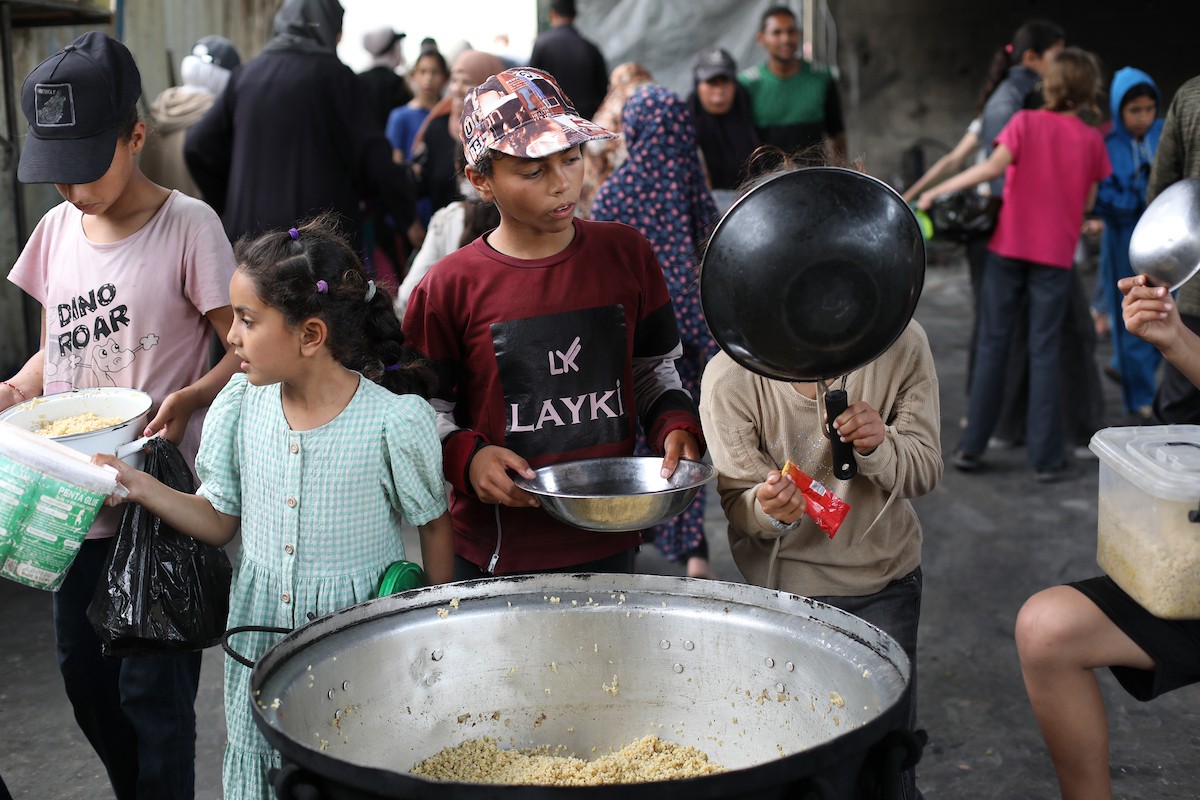 فلسطينيون نازحون، بينهم نساء وأطفال، يتجمعون لتلقي وجبات طعام من مطبخ خيري في مخيم النصيرات للاجئين وسط قطاع غزة، في 18 مايو/أيار 2026، وسط تراجع الإمدادات الإنسانية وخفض توزيع الوجبات اليومية من قبل منظمة «وورلد سنترال كيتشن». الصورة: حسن الجديدي
