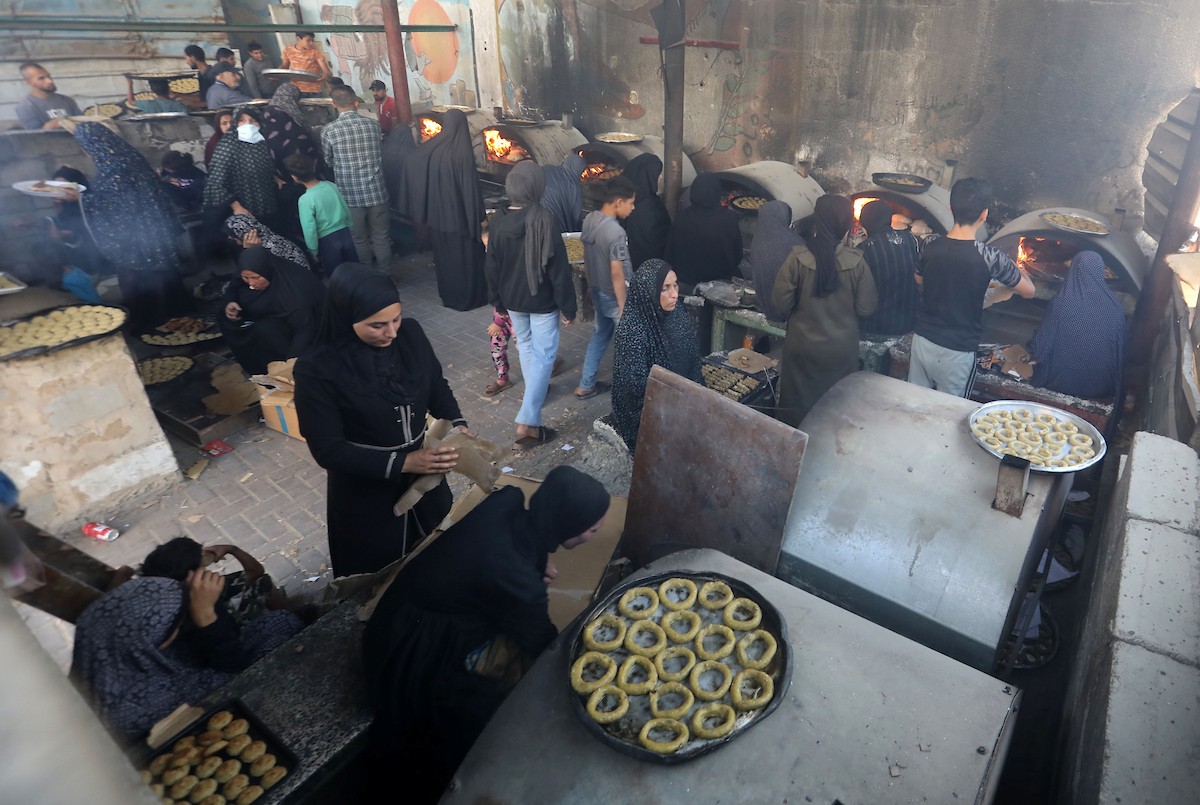 نساء فلسطينيات يُجهّزن ويخبزن كعكات العيد التقليدية على أفران مؤقتة داخل مأوى قرب منطقة “الخط الأصفر” شرق مدينة غزة، قبيل عيد الأضحى، 25 مايو/أيار 2026. تصوير: بلال أسامة
