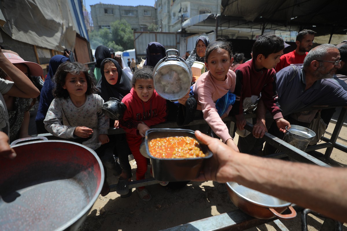 فلسطينيون نازحون، بينهم نساء وأطفال، يتجمعون لتلقي وجبات طعام من مطبخ خيري في مخيم النصيرات للاجئين وسط قطاع غزة، في 13 مايو/أيار 2026، وسط تراجع الإمدادات الإنسانية واستمرار الإغلاق الجزئي للمعابر الحدودية. تصوير: حسن الجديدي