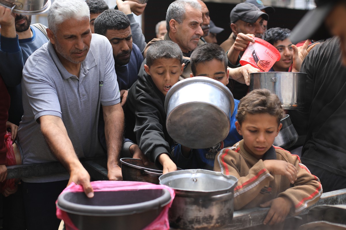 فلسطينيون بينهم نساء وأطفال يتلقون وجبات طعام من مطبخ خيري في النصيرات، وسط قطاع غزة، في 2 مايو/أيار 2026. (تصوير: حسن الجديدي)