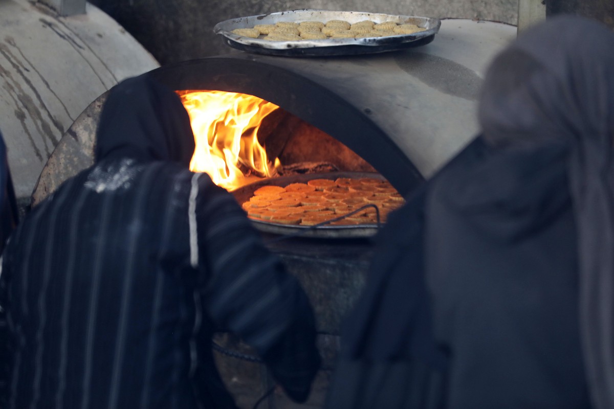 نساء فلسطينيات يُجهّزن ويخبزن كعكات العيد التقليدية على أفران مؤقتة داخل مأوى قرب منطقة “الخط الأصفر” شرق مدينة غزة، قبيل عيد الأضحى، 25 مايو/أيار 2026. تصوير: بلال أسامة