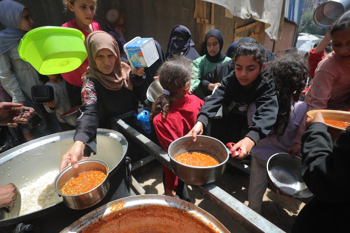 فلسطينيون نازحون، بينهم نساء وأطفال، يتجمعون لتلقي وجبات طعام من مطبخ خيري في مخيم النصيرات للاجئين وسط قطاع غزة، في 13 مايو/أيار 2026، وسط تراجع الإمدادات الإنسانية واستمرار الإغلاق الجزئي للمعابر الحدودية. تصوير: حسن الجديدي