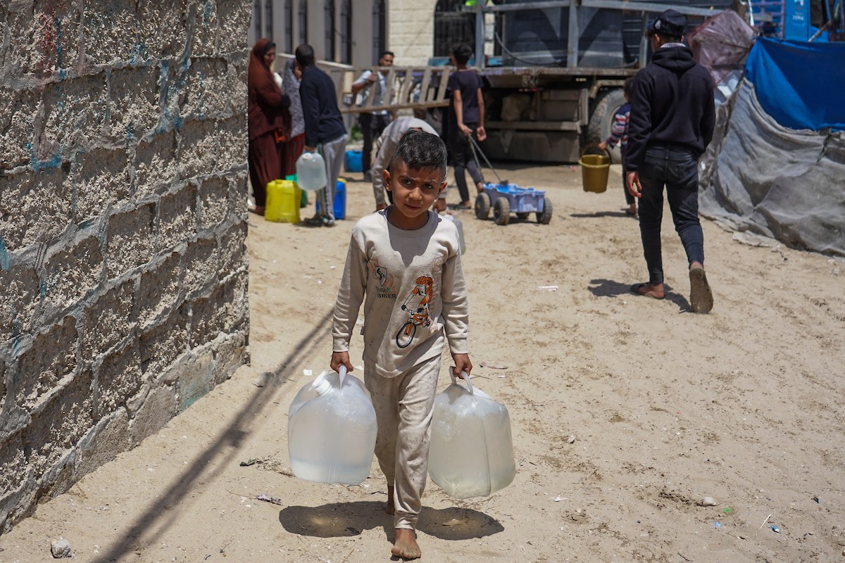 يحاول فلسطينيون نازحون، بينهم أطفال ونساء، جلب الماء من صهريج مياه متنقل في منطقة المواصي بخان يونس، جنوب قطاع غزة، 5 مايو/أيار 2026( صورة: رمزي أبو عامر)