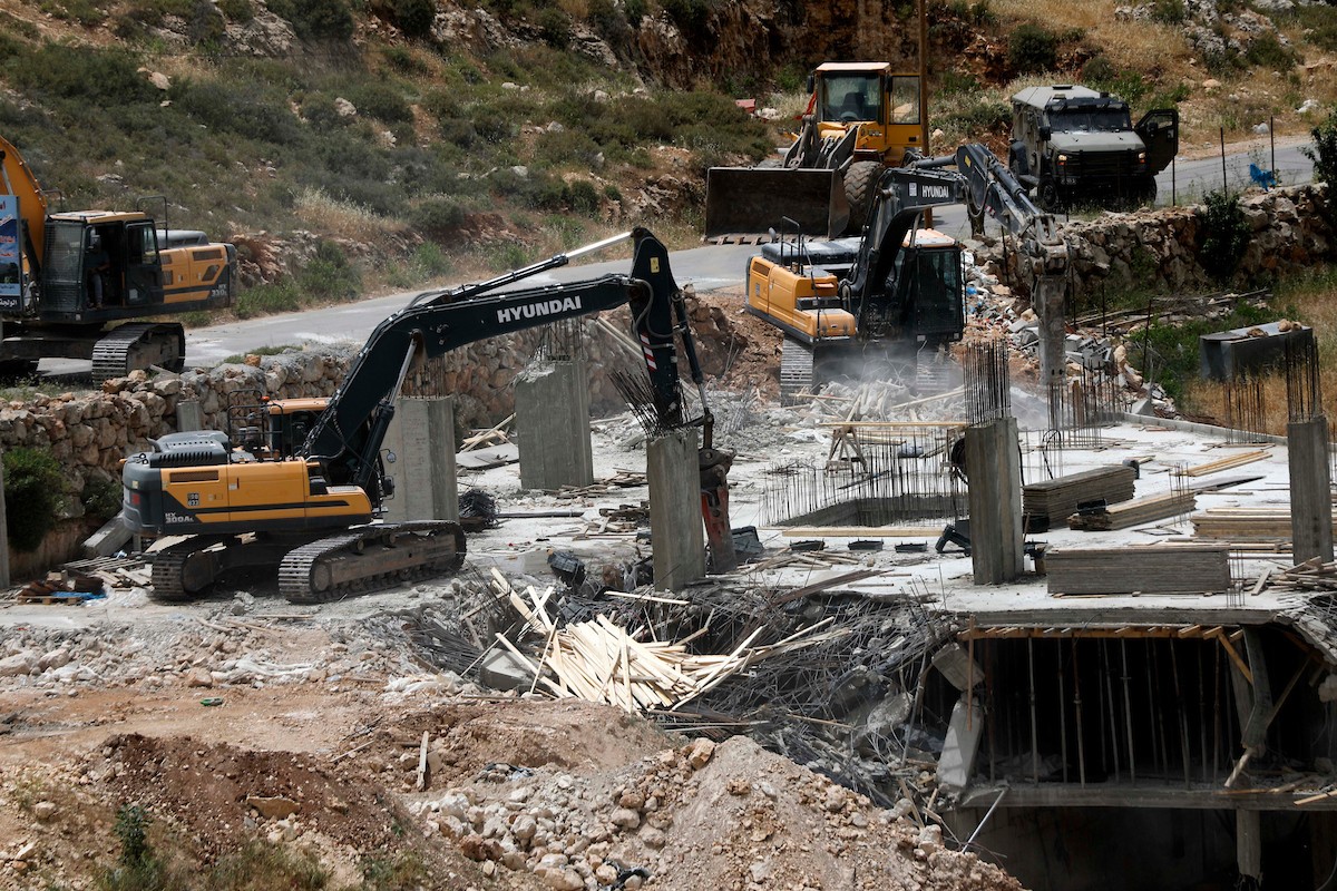 جرافات إسرائيلية تهدم مبنى سكنياً فلسطينياً قيد الإنشاء في بلدة الولجة غرب بيت لحم، في 18 مايو/أيار 2026، وسط انتشار قوات الاحتلال وتجمّع الأهالي لمتابعة عملية الهدم. الصورة: مأمون وزواز