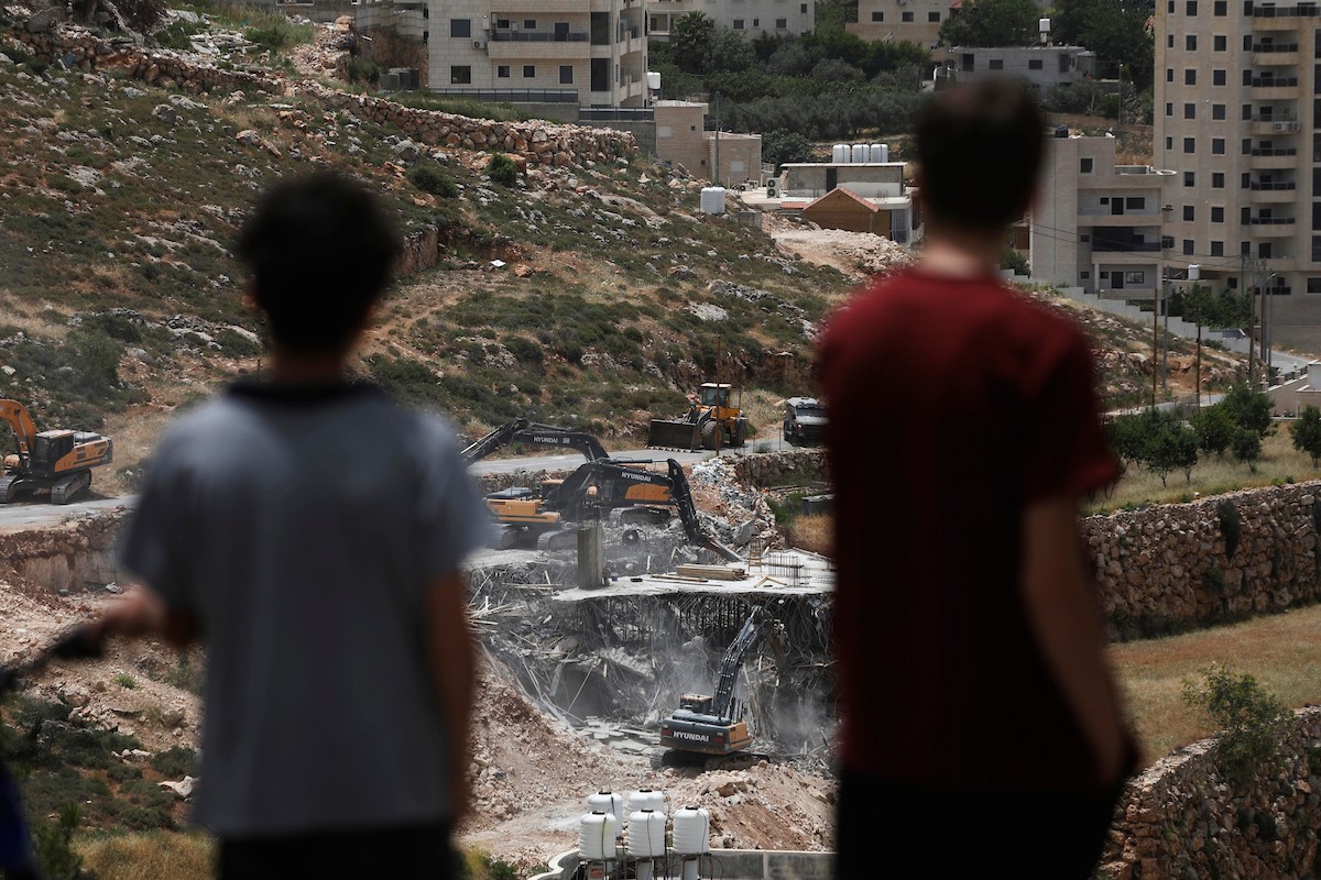 جرافات إسرائيلية تهدم مبنى سكنياً فلسطينياً قيد الإنشاء في بلدة الولجة غرب بيت لحم، في 18 مايو/أيار 2026، وسط انتشار قوات الاحتلال وتجمّع الأهالي لمتابعة عملية الهدم. الصورة: مأمون وزواز