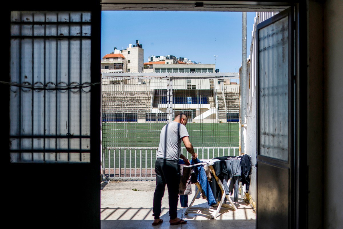 رجل فلسطيني من قطاع غزة عالق في الضفة الغربية المحتلة ينشر ملابسه على رفّ الغسيل لتجف تحت أشعة الشمس في مخيم بملعب نابلس لكرة القدم وسط مدينة نابلس بالضفة الغربية. 7 آيار 2026. (أ ف ب).jpg
