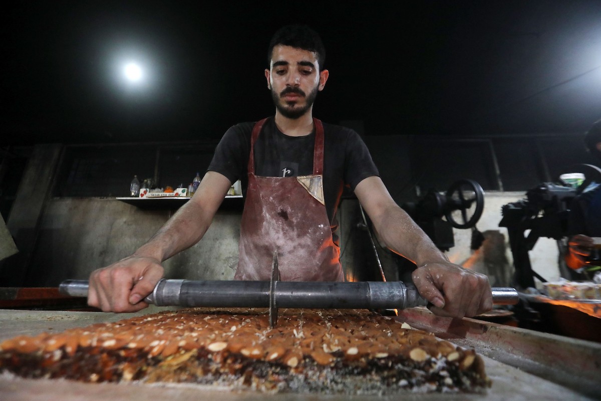 عمال فلسطينيون ينتجون حلوى “الحلقوم” التقليدية داخل مصنع متضرر في حي الدرج شرق مدينة غزة، قبيل عيد الأضحى المبارك، في 24 أيار/مايو 2026، بعد استئناف العمل بإمكانيات محدودة جراء أضرار الحرب وتراجع القدرة الشرائية للسكان. تصوير: بلال أسامة